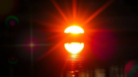 A captivating image showcases a vibrant sunset reflected in a tranquil pond.  Bright lens flares and complementary colors cre