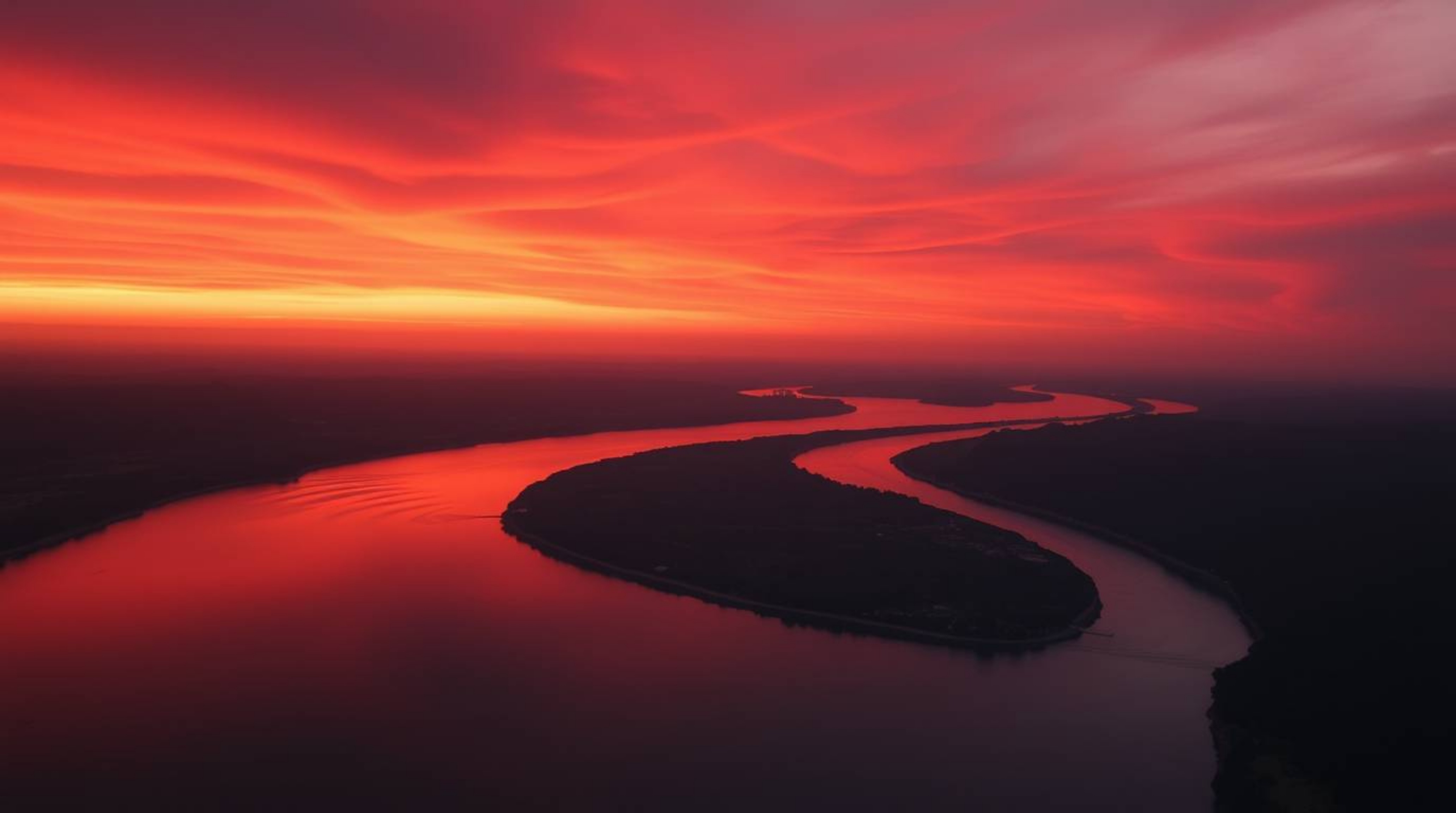 A captivating cinematic photograph showcasing a winding river glowing under a dramatic orange-pink sky.  The film-like compos