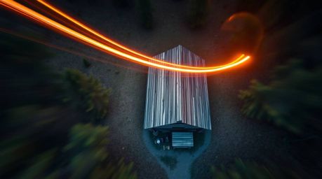 A captivating long exposure photograph reveals an old wooden cabin nestled deep within a forest at sunset.  Shot from a bird'