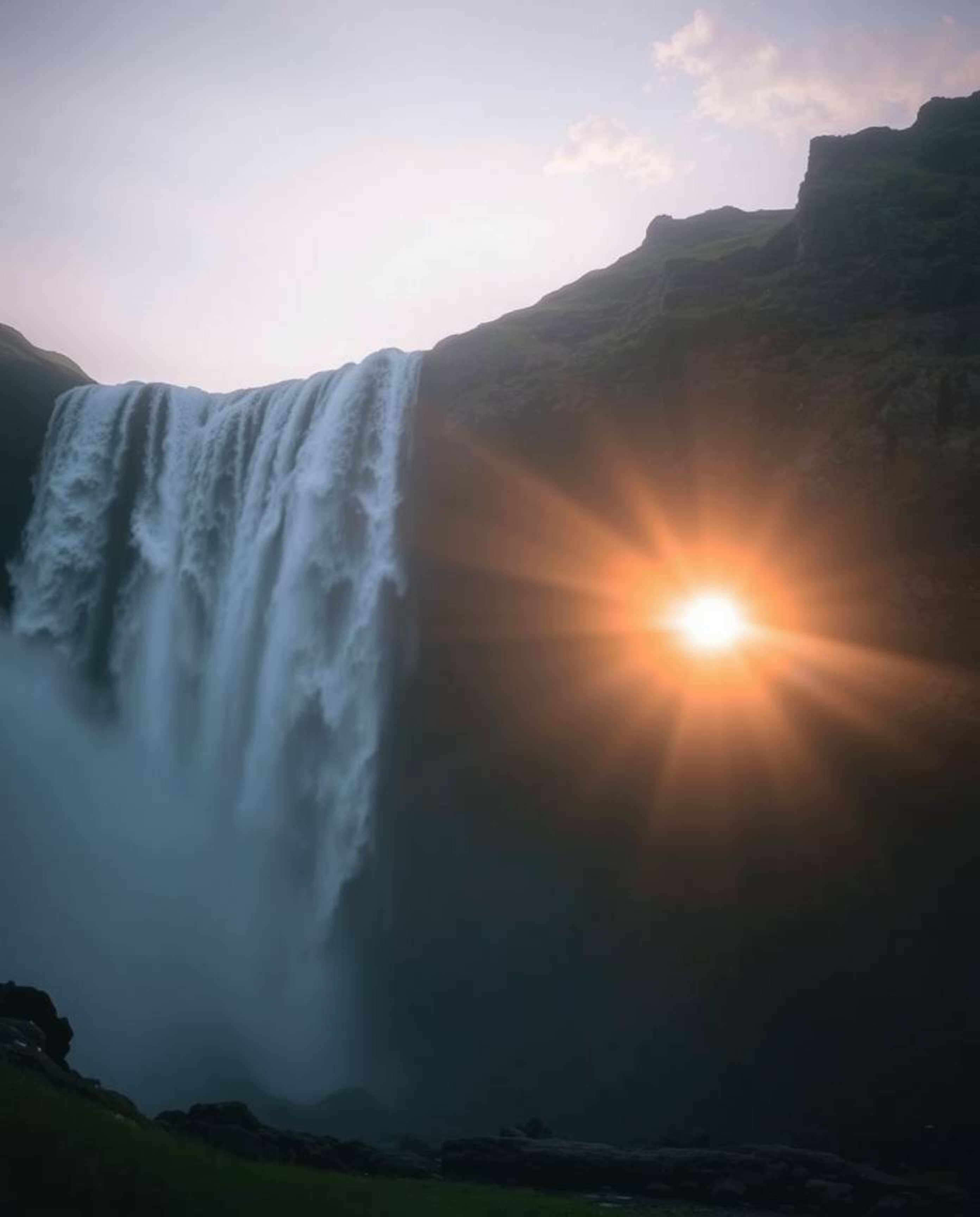 This is an ethereal photograph of a sun setting behind a dramatic waterfall. The image conveys a profound spiritual vibe, cha