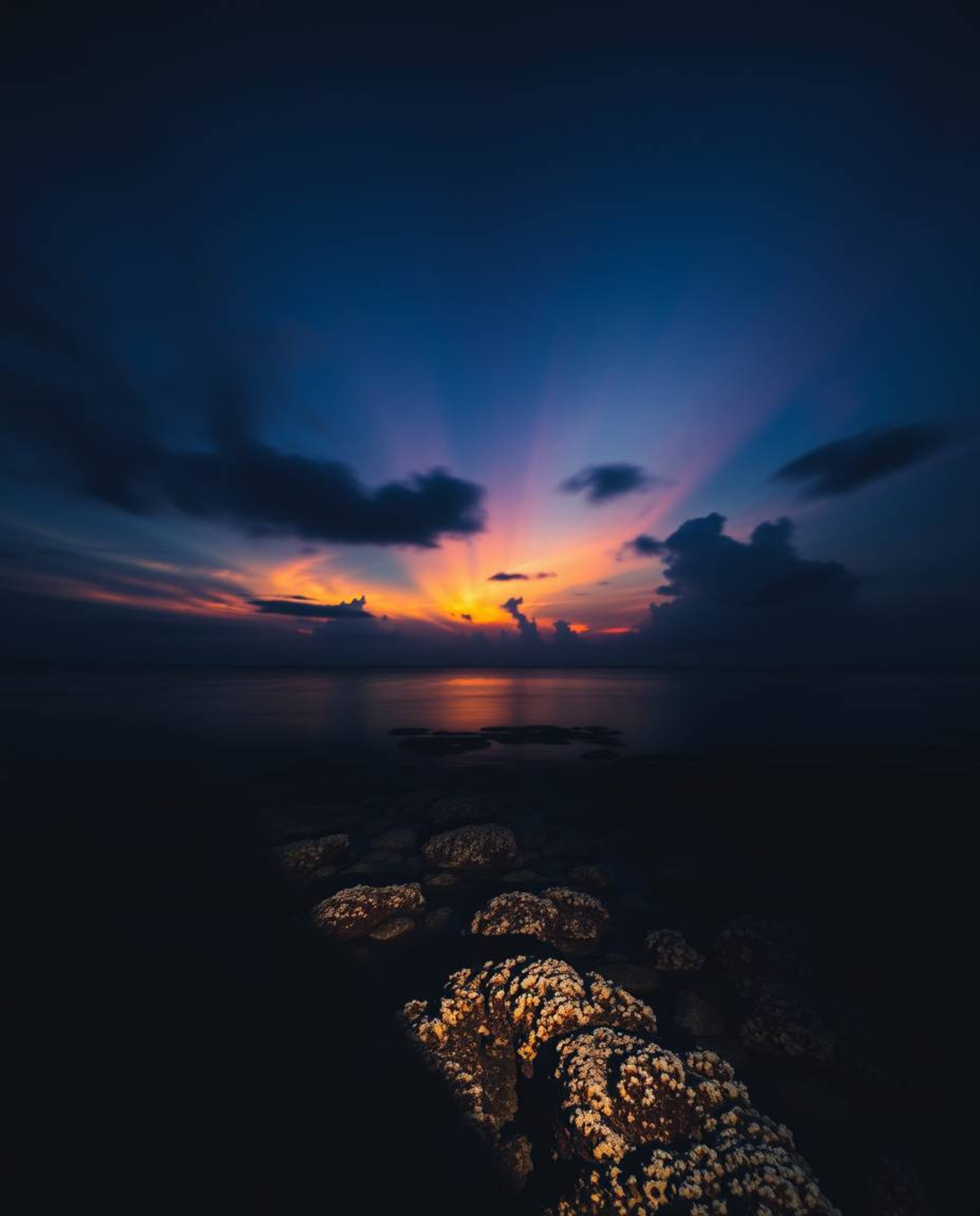 Long-exposure photography captures a colorful sky over a coral reef at low tide, employing high-contrast, low-key lighting to