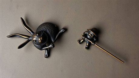 A bronze sculpture depicting a top-down view of a wacky rabbit outrunning a hunter in a slapstick chase. The textured surface