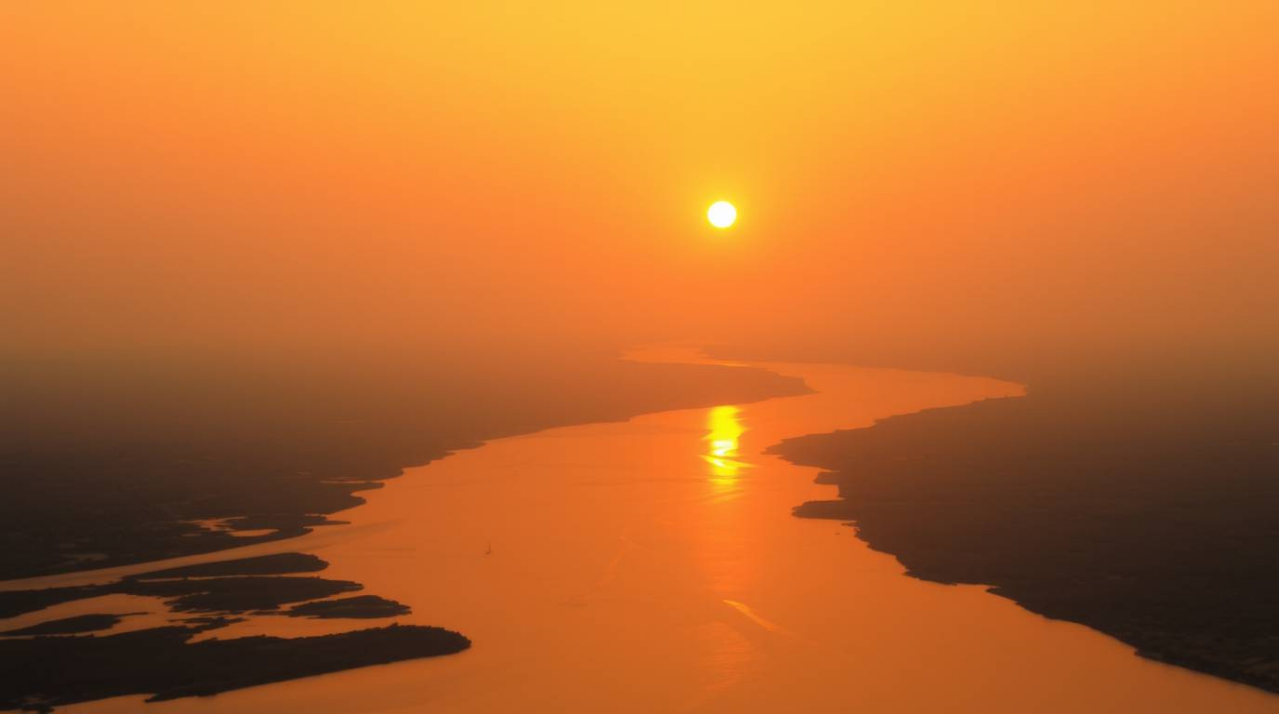 A captivating image of a river delta bathed in the warm glow of twilight.  Soft reds, oranges, and yellows paint the scene in