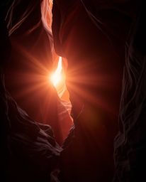 A dramatic and ethereal sunset illuminates sandstone cliffs in a canyon. The scene is defined by high-contrast lighting, a su