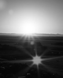 A striking black and white photograph captures a sunrise over a desolate, war-torn landscape. The image, graceful and elegant