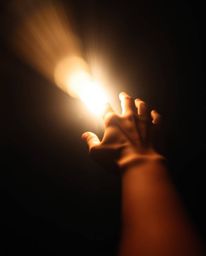 This dynamic light art image captures the essence of reaching for hope. A hand extends toward a vibrant light source emerging
