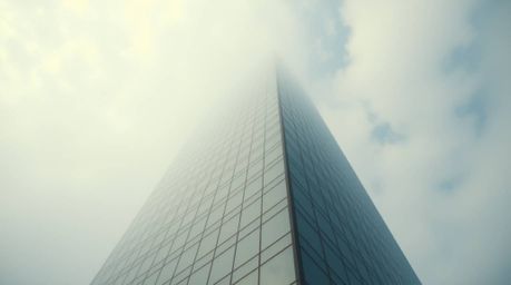 This image captures a modern glass building seemingly dissolving into a hazy sky, where soft clouds gently blend into its str