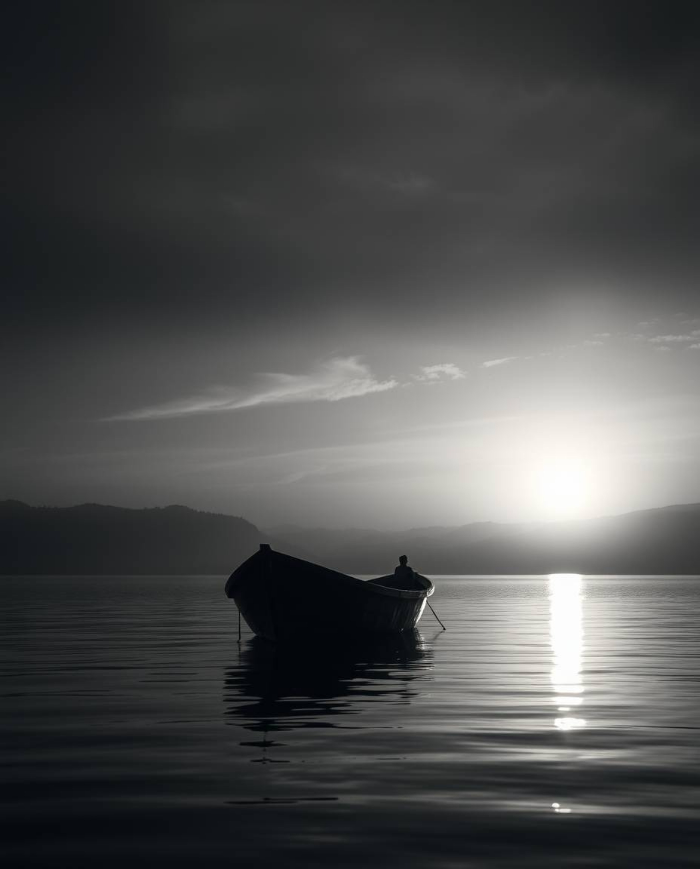 This is a classic black and white image of a boat adrift on a lake at sunset, creating a timeless and elegant, yet mystic and