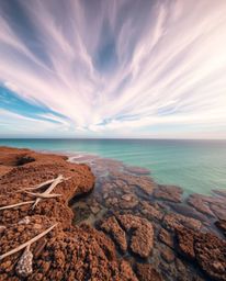 This artwork presents a high-angle perspective of a colorful sky over a coral reef during low tide. The piece is characterize