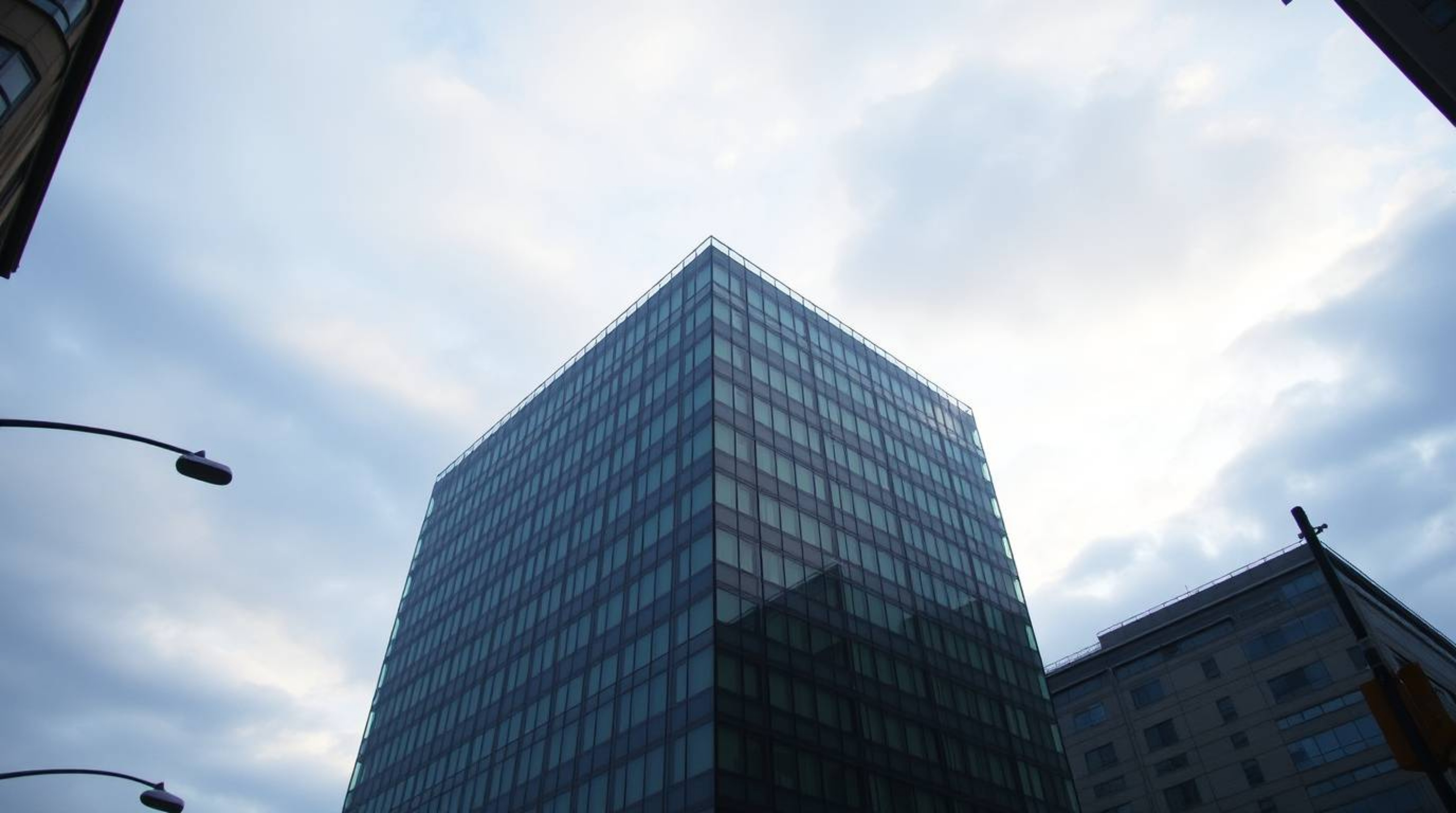 A captivating street photograph showcases a contemporary glass building seemingly dissolving into a serene sky painted with s
