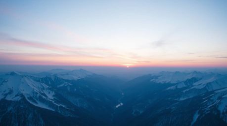 Capture the serene beauty of snow-covered mountains bathed in the soft hues of a pastel sunset.  This high-angle perspective 
