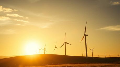 This photograph showcases a dramatic cinematic sunset behind a row of wind turbines situated on a hill. Bathed in the warm, g