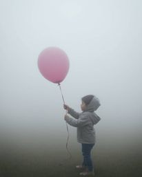 A captivating image of a child holding a balloon in a thick, foggy setting. The soft, dreamy atmosphere and low visibility cr