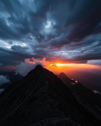 Witness a dramatic sunset from a high alpine peak amidst intense weather and stormy skies. This powerful scene is filled with