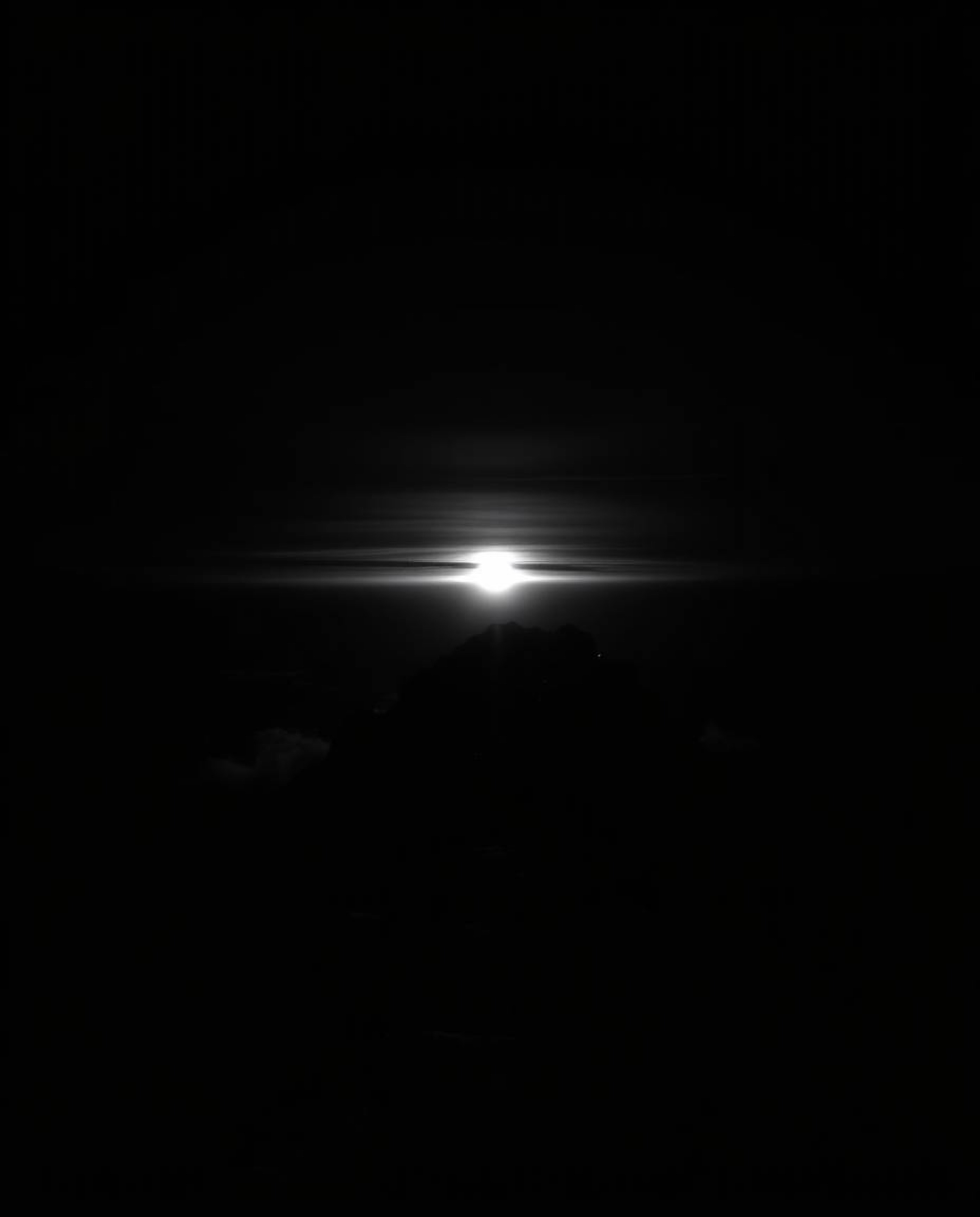 This is a high-contrast black and white photograph depicting a moody sunset from a high alpine peak. The composition uses low