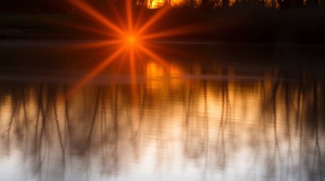 Capture the serene beauty of a golden hour sunset reflected in a calm pond. This long exposure photograph showcases vibrant c