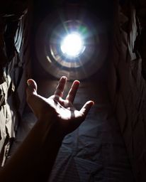A captivating image depicting a hand emerging from darkness towards a light source.  Crafted from layered papier-mâché, the a