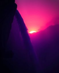 A dramatic waterfall is silhouetted against a sunset, where deep ultraviolet hues dominate the soft cinematic haze. This high