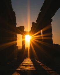A creative light art piece depicting a sunset casting shadows through ancient stone ruins. The scene is bathed in a warm gold