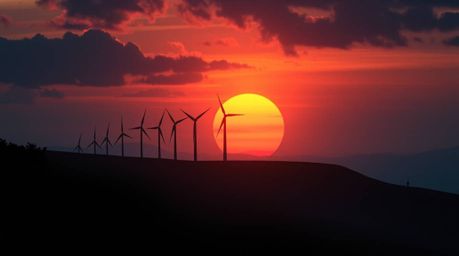 A captivating film still depicting a dramatic sunset behind a row of wind turbines perched on a hill.  The image boasts a cin