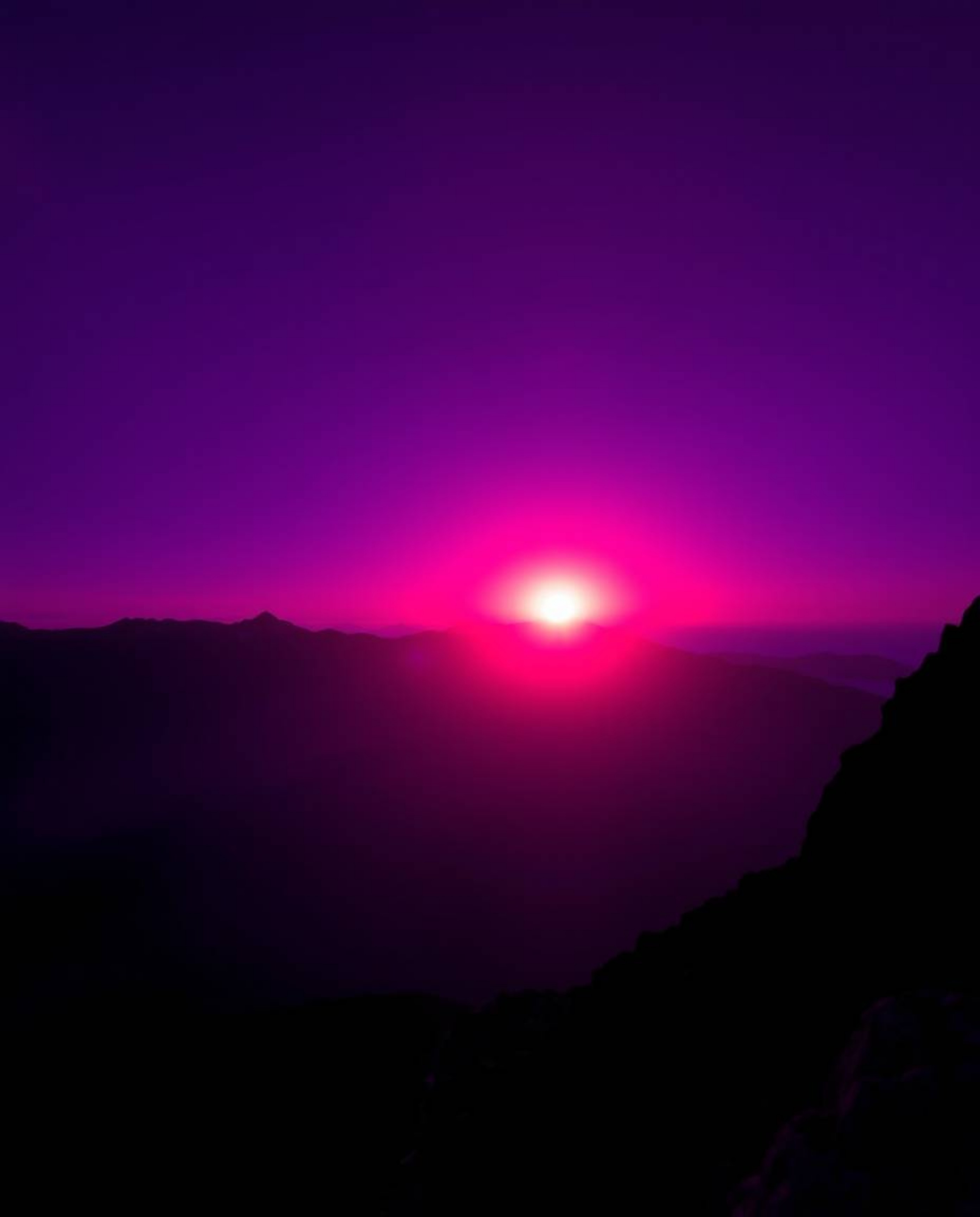This is a captivating long-exposure photograph of a sunset viewed from a high alpine peak, rendered in deep ultraviolet hues 