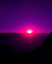 This is a captivating long-exposure photograph of a sunset viewed from a high alpine peak, rendered in deep ultraviolet hues 
