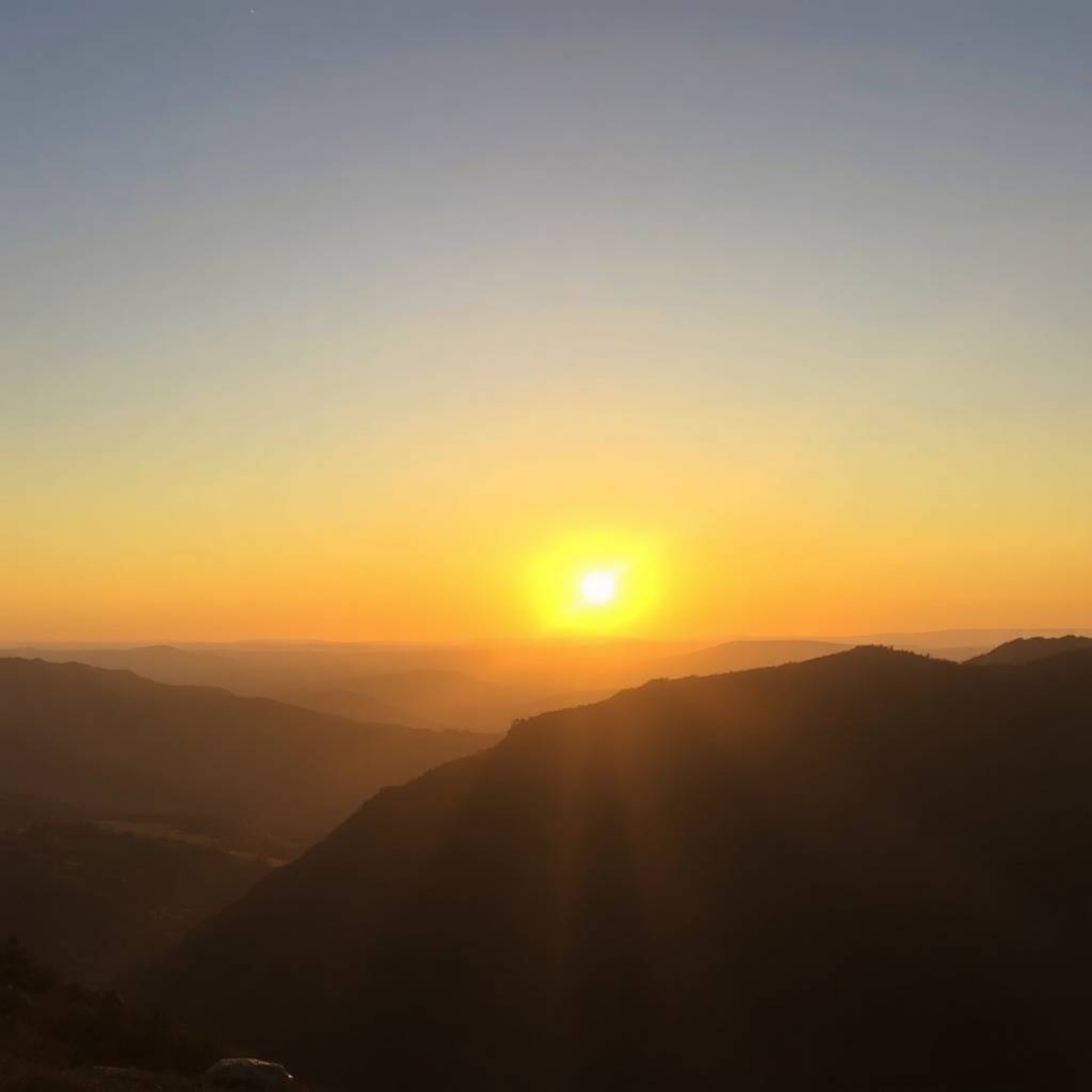 This photograph captures the serene beauty of a sunset over a quiet mountain valley. Bathed in the warm, golden hour light, t