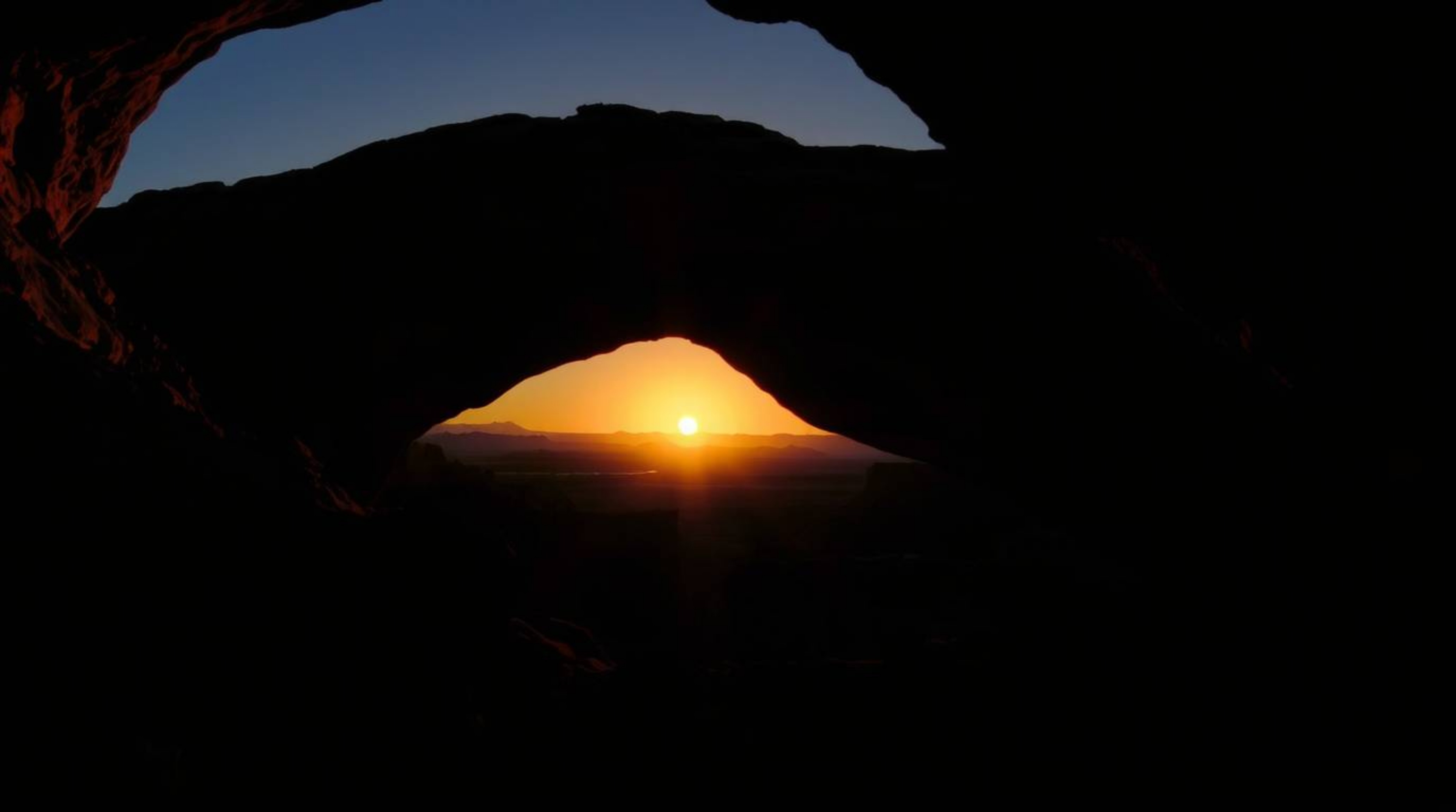 A captivating image of a desert sunset dramatically showcased through a natural rock arch.  High-contrast, low-key lighting c