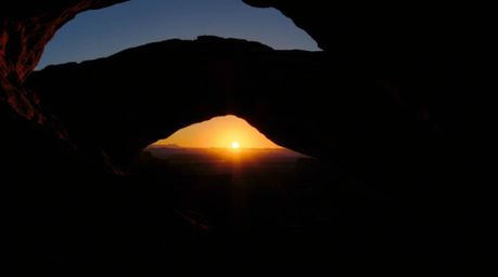 A captivating image of a desert sunset dramatically showcased through a natural rock arch.  High-contrast, low-key lighting c