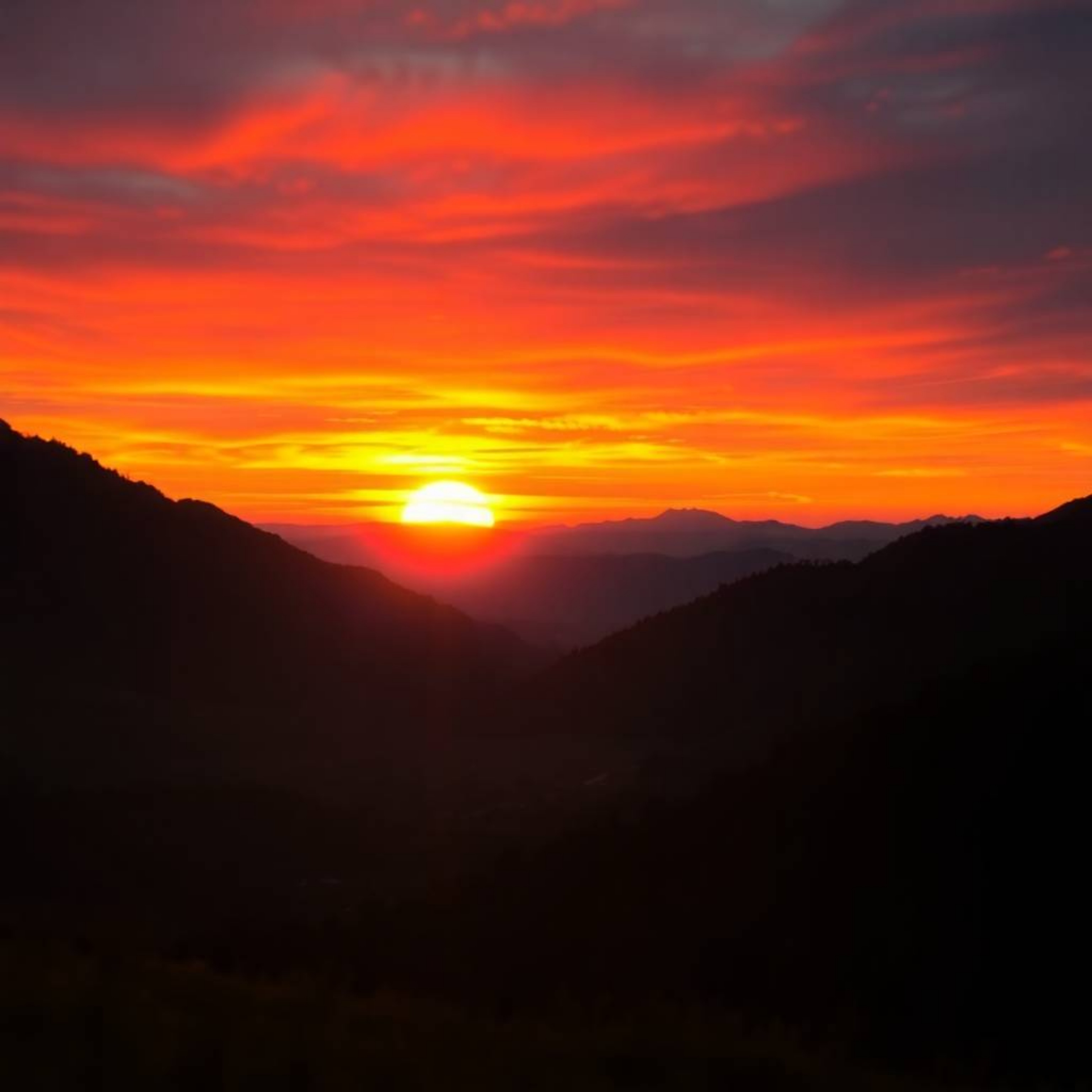 Experience the breathtaking beauty of a sunset over a serene mountain valley. Vivid electric colors paint the sky as warm can