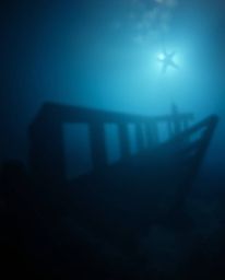 An underwater shipwreck scene is bathed in a gentle, soft light, enhanced by a beautiful blurred bokeh effect. This lighting 