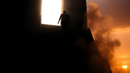 A silhouetted figure ascends a stone staircase bathed in a divine light beam, back lit against a moody sunset sky filled with