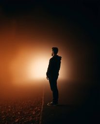 A sharply focused individual stands at a tunnel's entrance, gazing towards a source of light.  The background is artistically