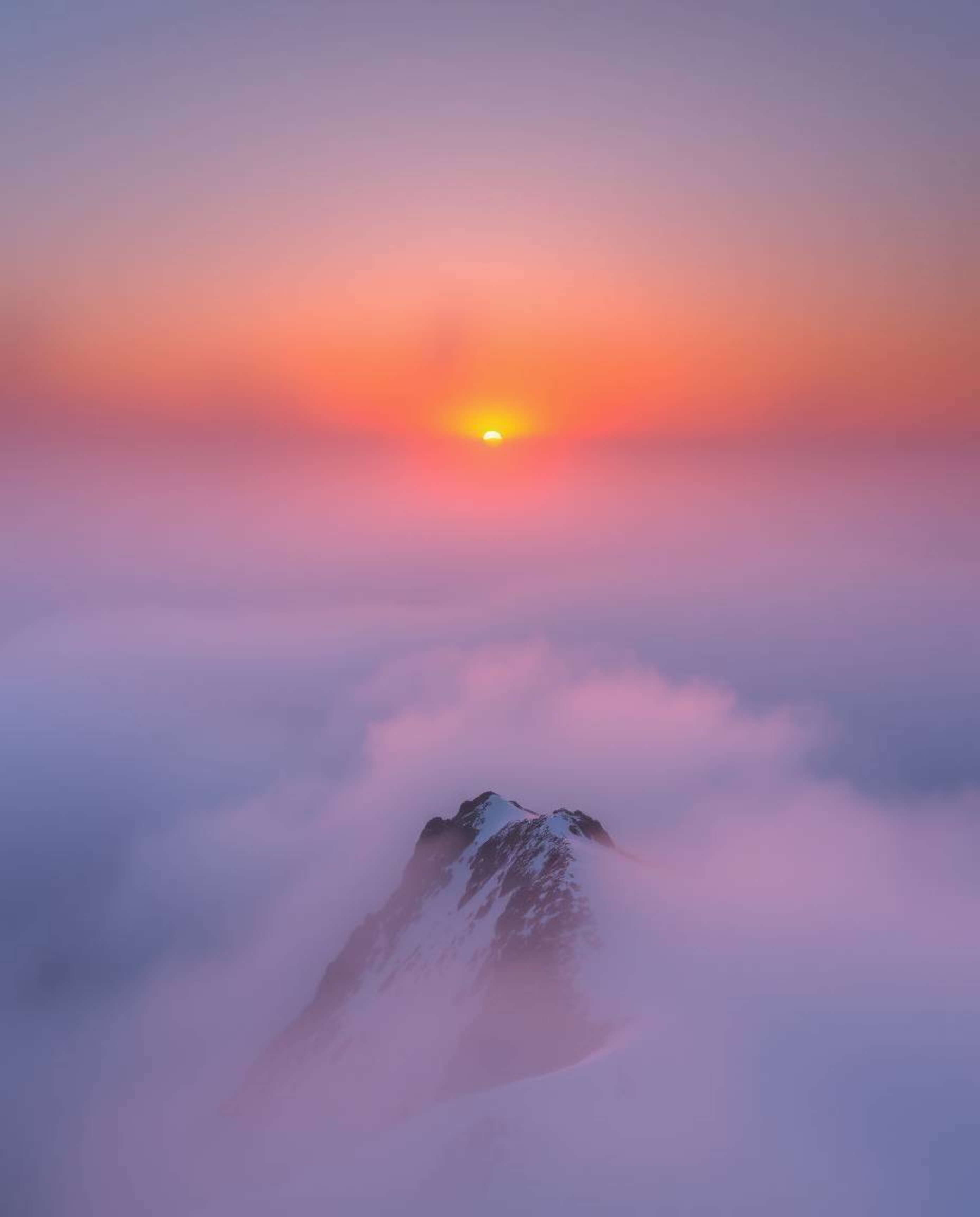 Experience a sunset from a high alpine peak, where the view is almost entirely obscured by thick fog. This atmospheric scene 