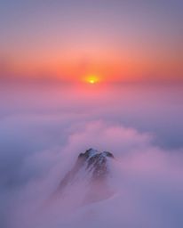 Experience a sunset from a high alpine peak, where the view is almost entirely obscured by thick fog. This atmospheric scene 