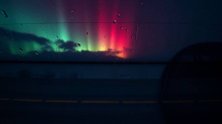 A captivating overhead shot depicts a wet, rainy scene with the mesmerizing Northern Lights emerging over a vibrant sunset sk