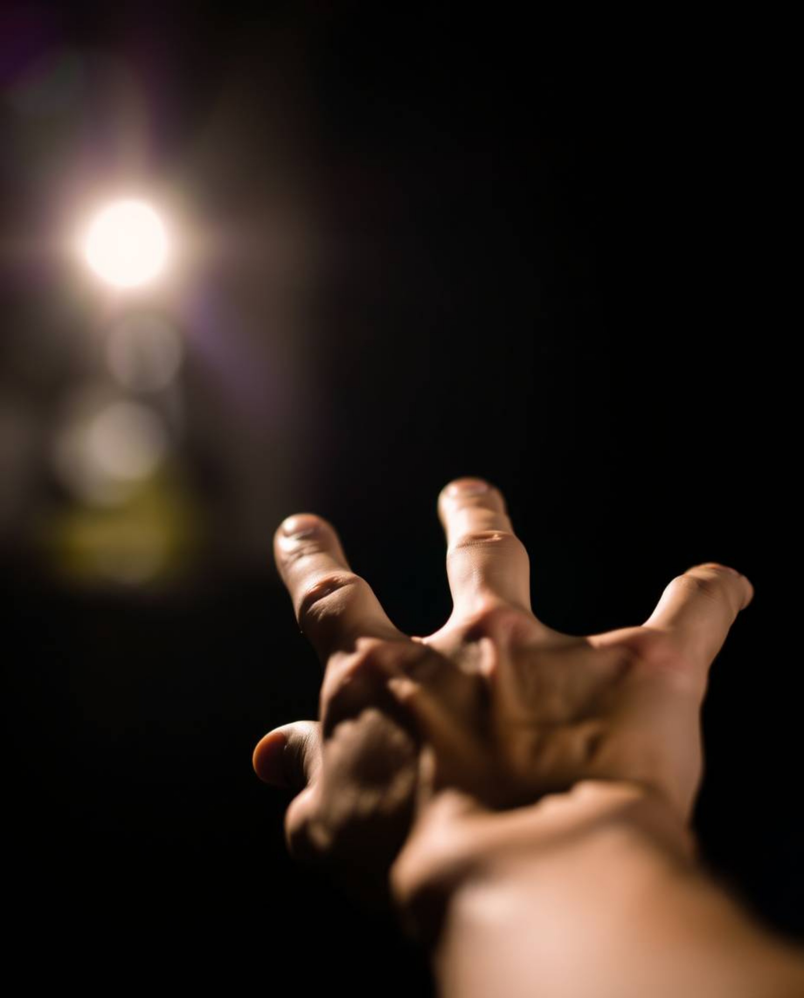An evocative image depicting a sharp hand reaching towards a light source from a dark, blurred background.  The soft focus an