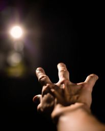 An evocative image depicting a sharp hand reaching towards a light source from a dark, blurred background.  The soft focus an