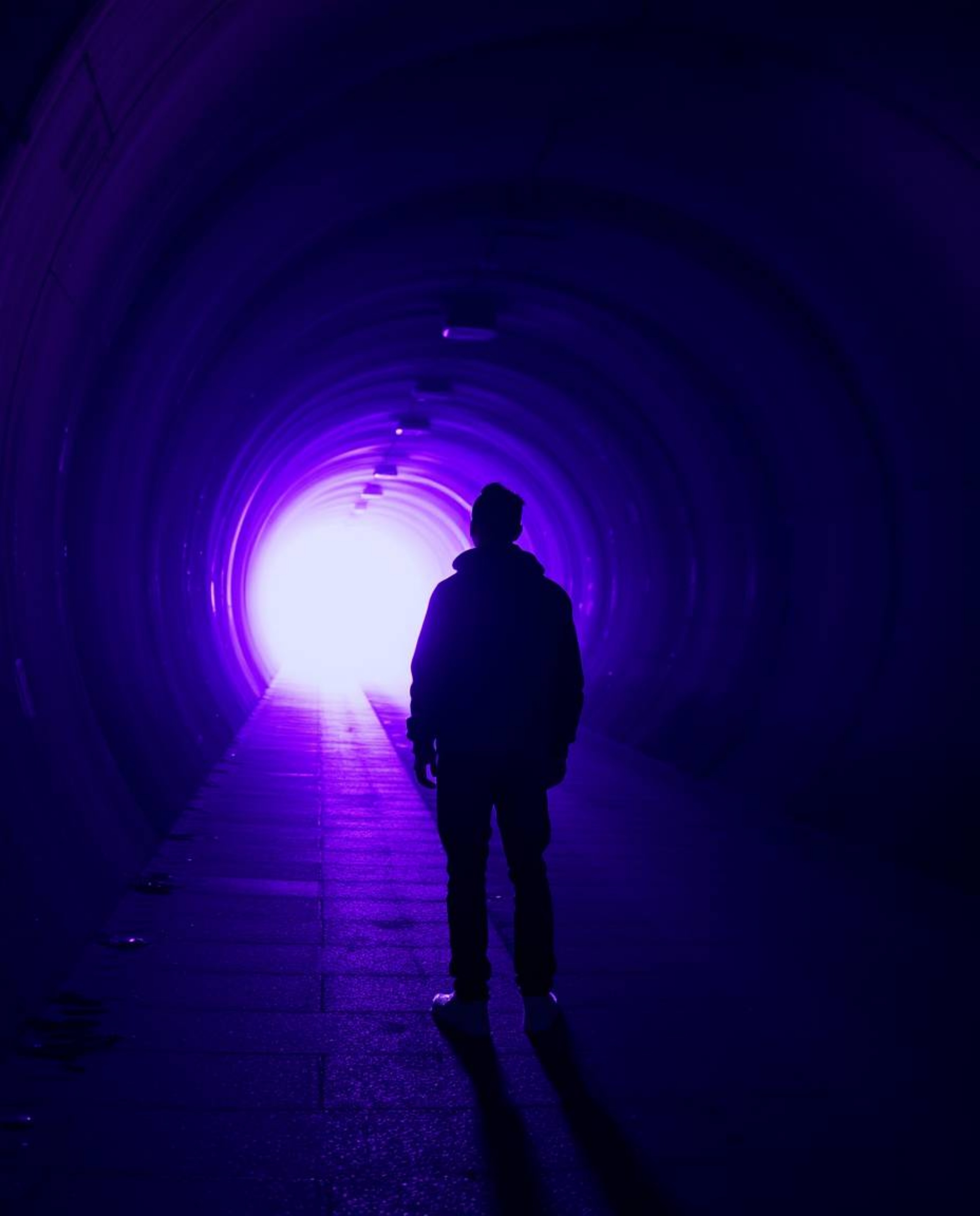A captivating image depicts a person bathed in deep ultraviolet hues, standing at the edge of a tunnel and gazing towards a b