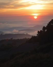 An unusual, original fine art photograph depicting a dramatic sunset over misty Tuscan hills. High contrast lighting creates 