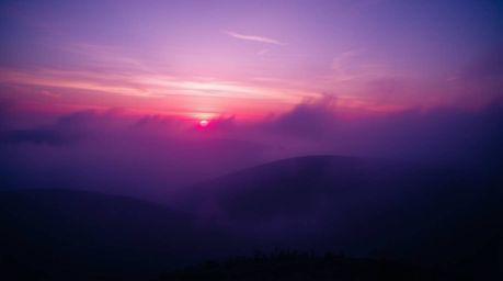 A dynamic image capturing fog-covered hills at sunset, rendered in deep ultraviolet hues. The scene is characterized by blurr