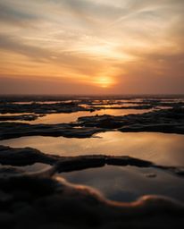A high-resolution stock photo of commercial quality captures a sunset sky mirrored in the serene tidal pools of a beach. The 