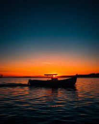 High-contrast, low-key lighting accentuates a boat drifting on a lake during sunset. The intentional use of deep shadows crea
