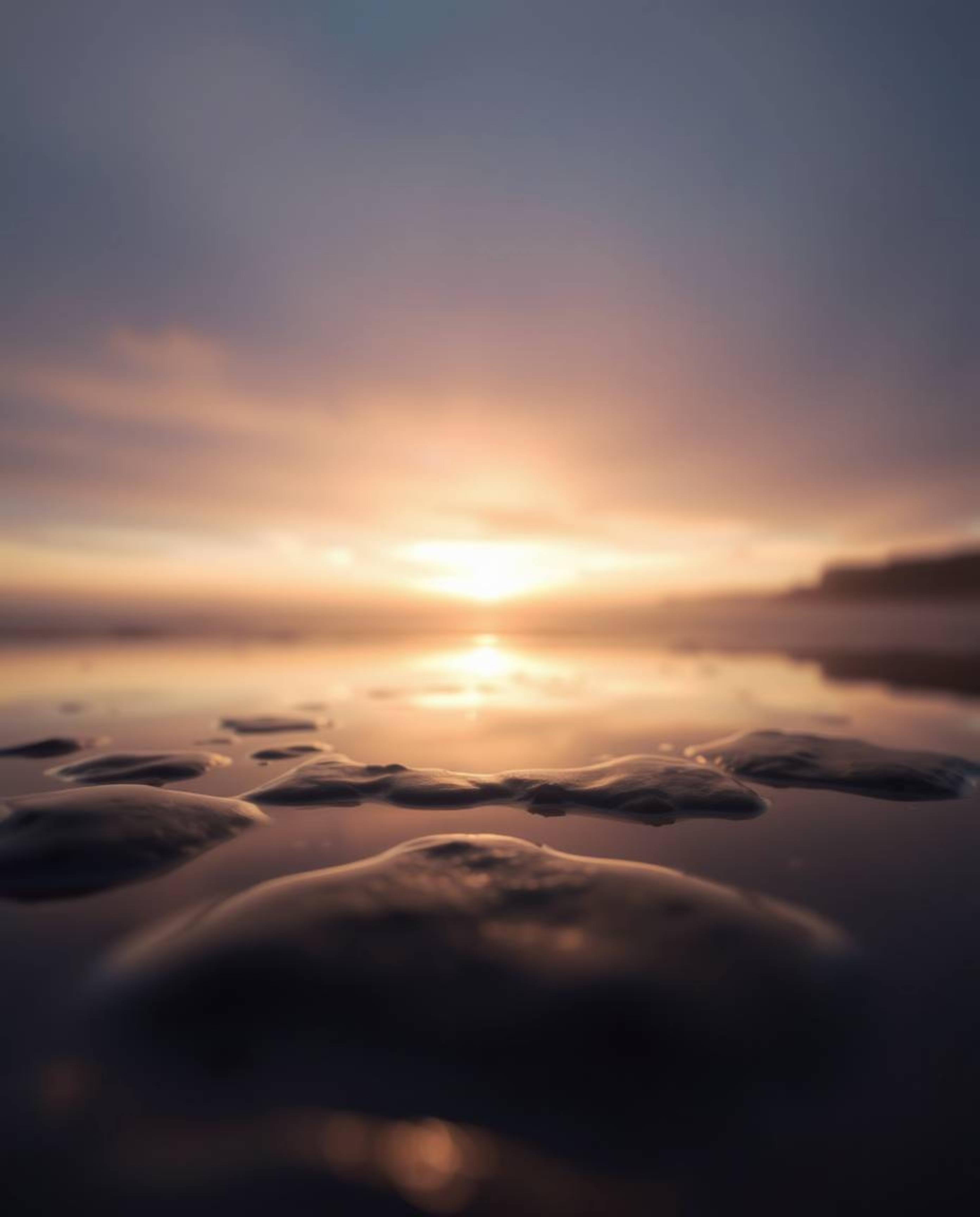 A soft cinematic sunset sky is beautifully mirrored in the tidal pools on a beach. This photograph uses a soft focus and a ha