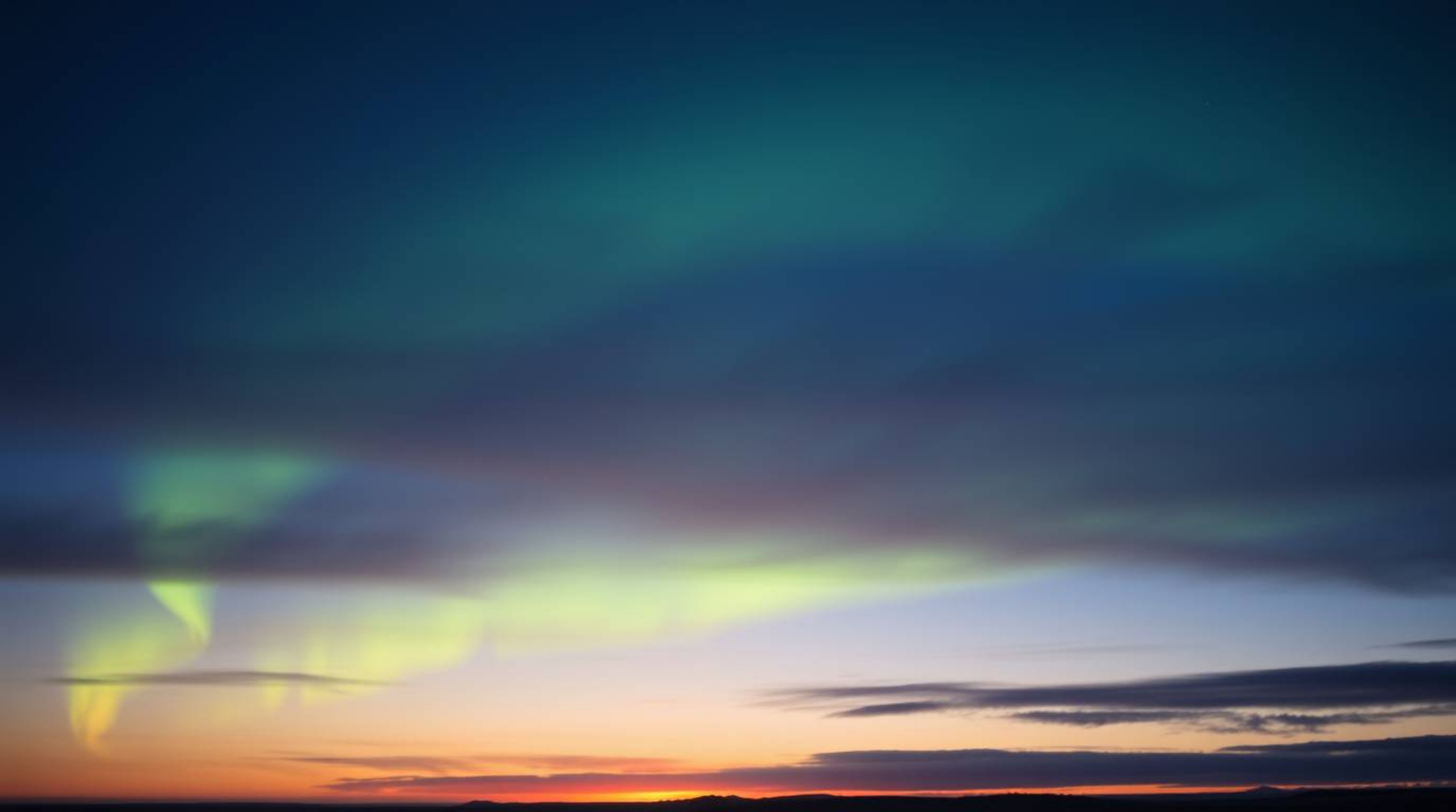 A captivating image depicting the soft, dreamy emergence of the Northern Lights over a sunset sky.  Low contrast and hazy sof
