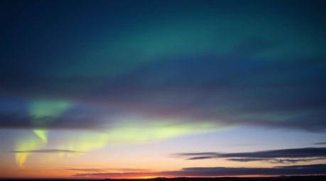 A captivating image depicting the soft, dreamy emergence of the Northern Lights over a sunset sky.  Low contrast and hazy sof