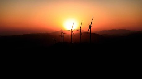 A captivating architectural photograph showcases a breathtaking sunset casting an ethereal glow behind a row of wind turbines