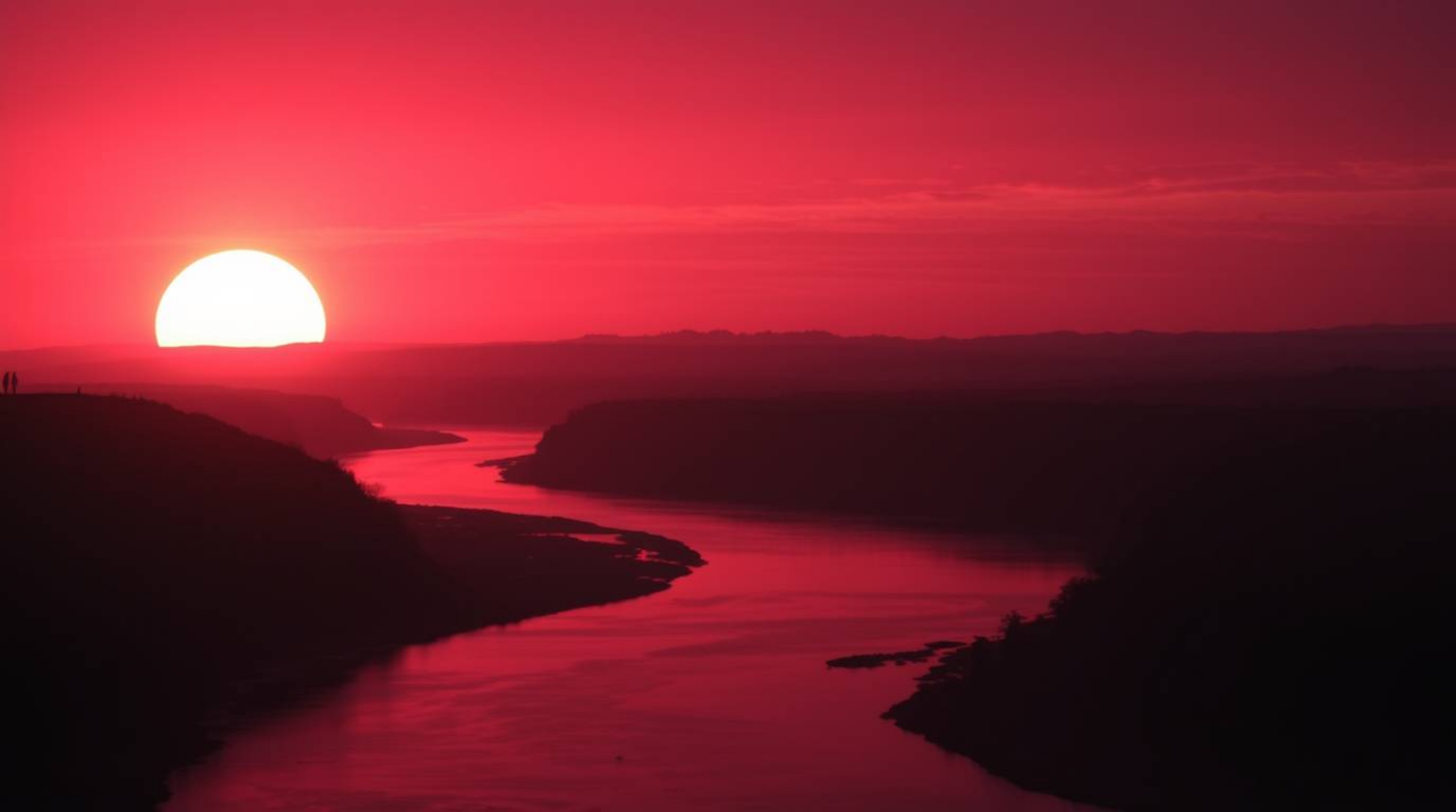 This professional fine art photography captures a winding river bathed in the dramatic glow of an orange-pink sky. Silhouette