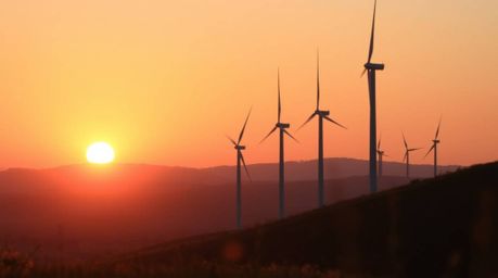 A stunning close-up shot captures the vibrant details of a sunset behind a row of wind turbines perched atop a hill. The imag
