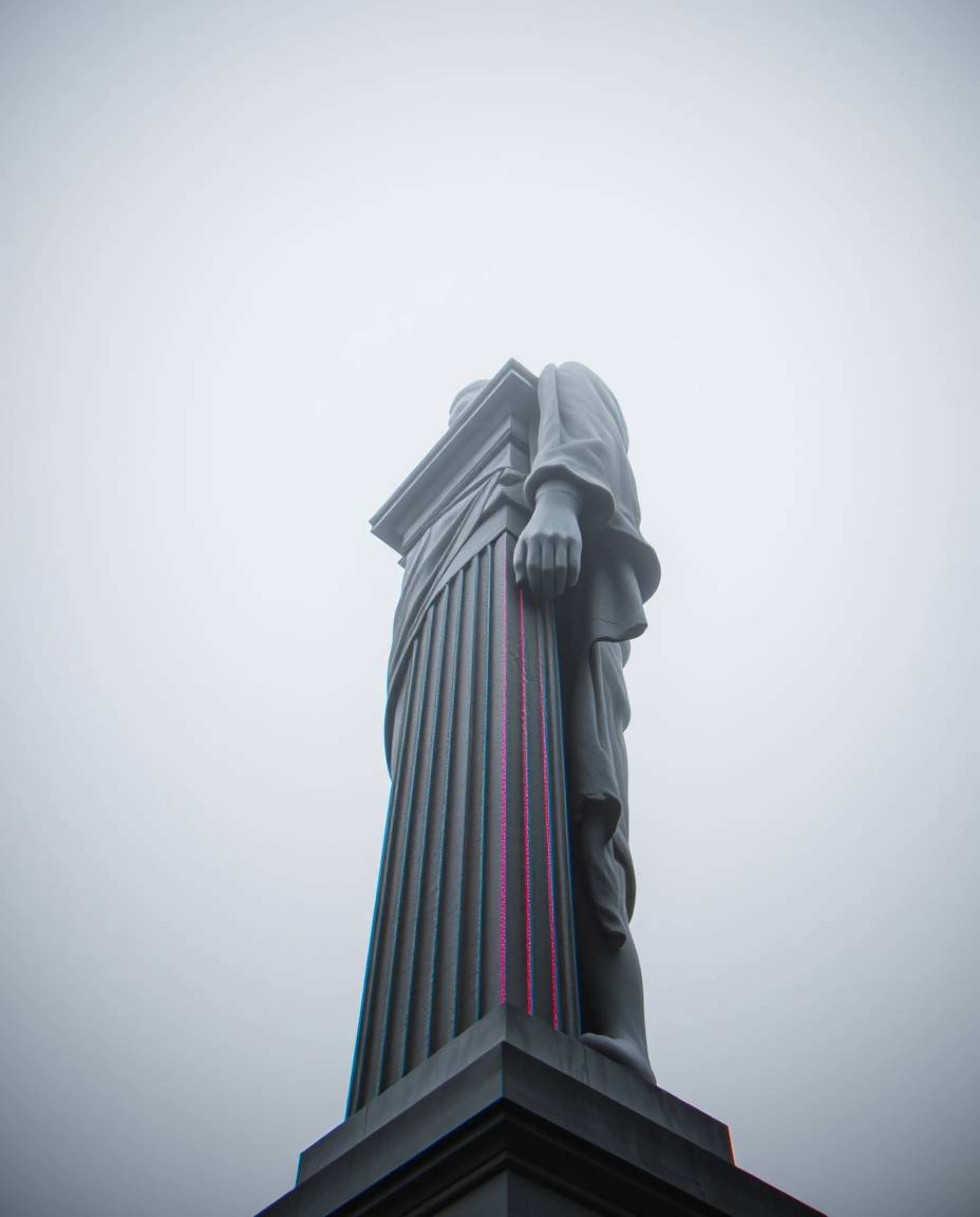 A high-angle, monochromatic shot depicts a classical sculpture enveloped in thick fog, showcasing a striking colorful glitch 